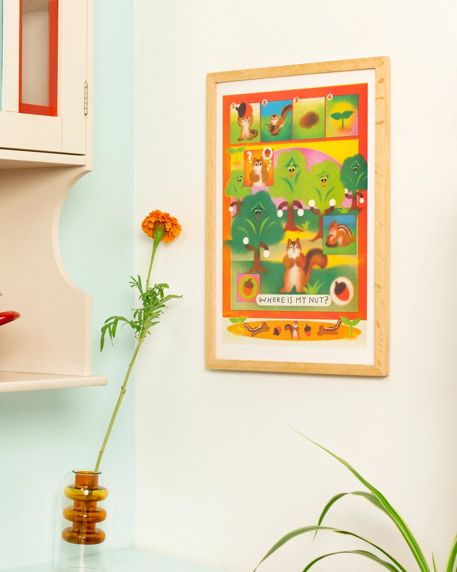 The Little Gardener poster framed in light wood, hung above a shelf with a flower in a vase