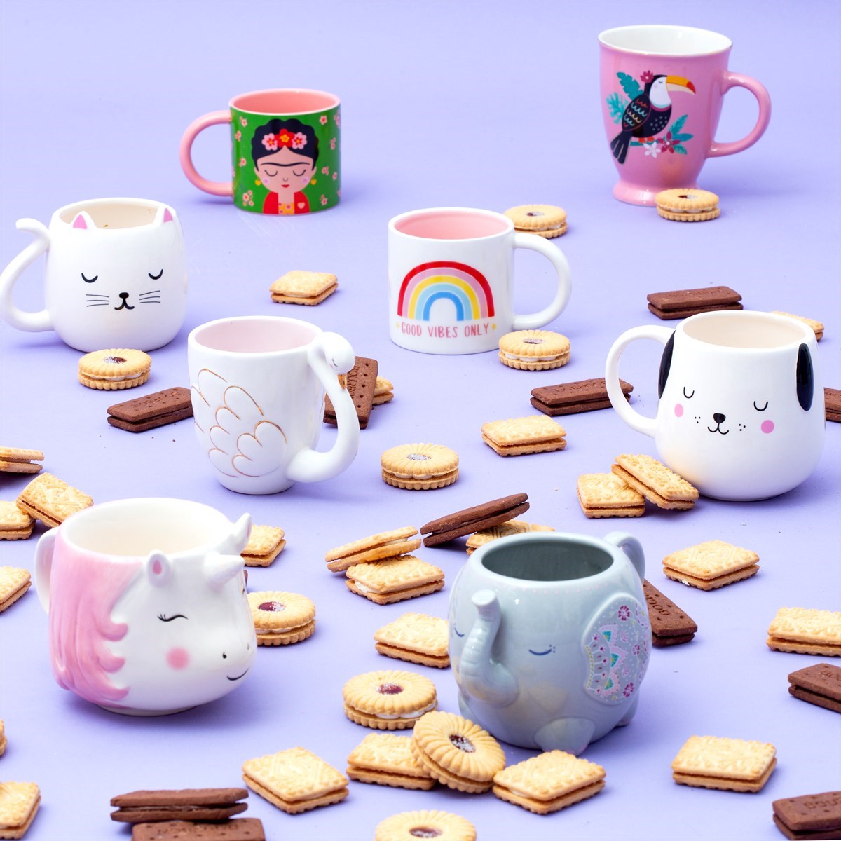 The Frida mug among a group of animal- and rainbow-themed mugs, surrounded by biscuits on a lilac background.