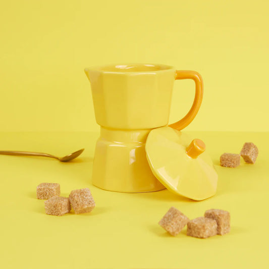 Yellow Moka Cup on a yellow background, lid removed, with brown sugar cubes