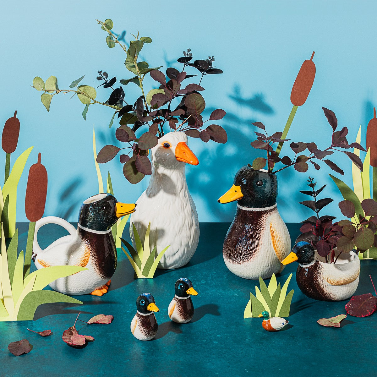 Oca vase among a group of duck and goose-shaped vases with plants on a blue background.