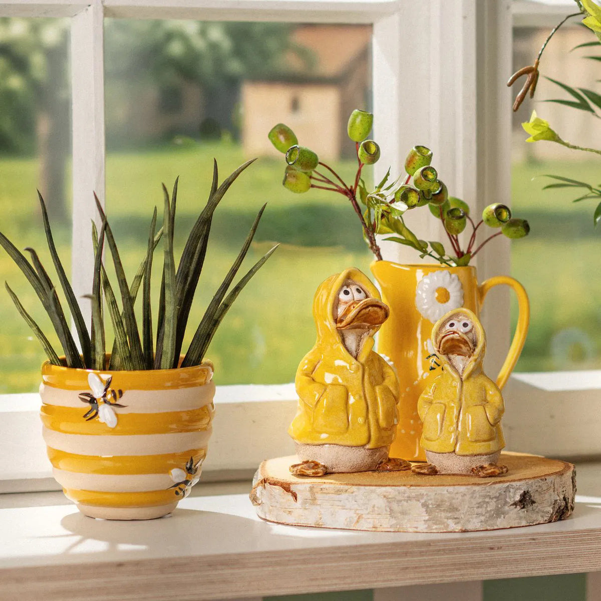 Alveare vase in yellow with painted bees, next to two chick figurines in raincoats on wood.