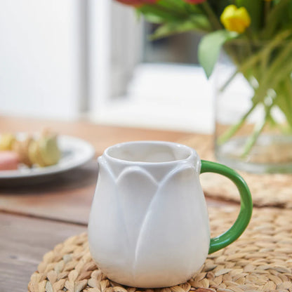 White Tulip mug on a table with a vase of flowers in the background