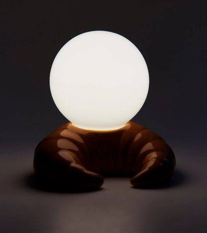 Croissant lamp lit in the dark, chocolate-toned base with the sphere glowing