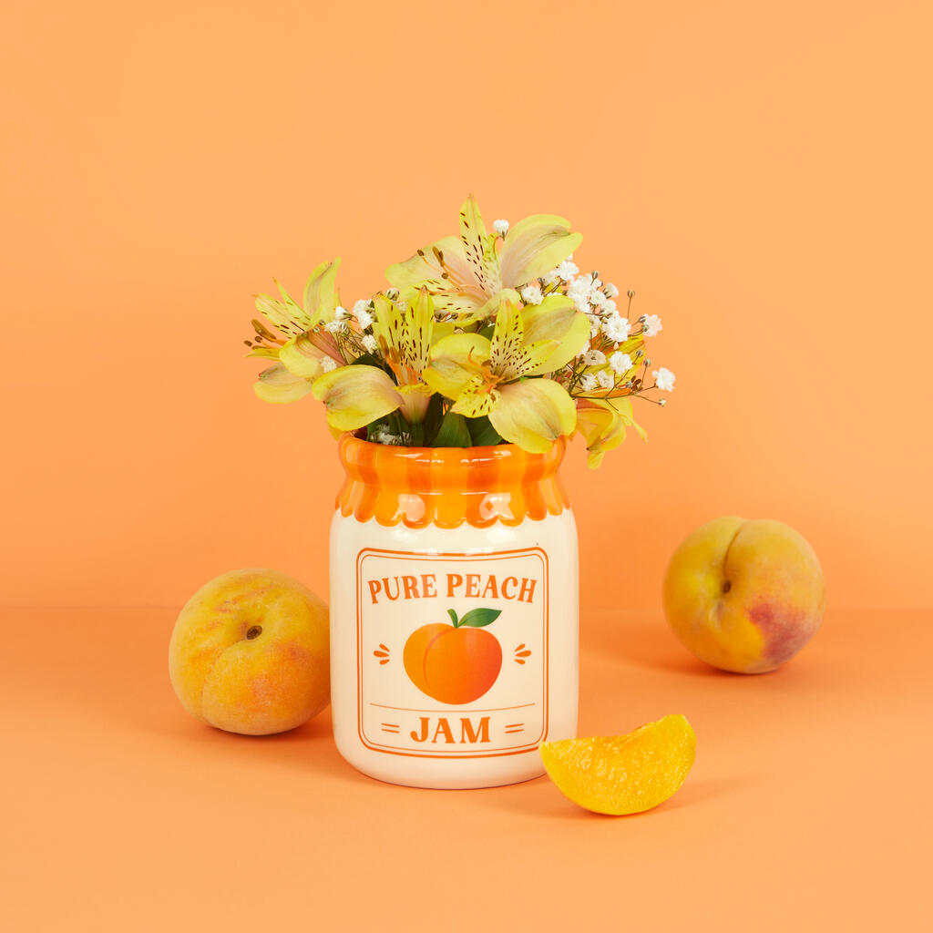 Jam vase, peach version with flowers, between two whole peaches and a wedge, orange background