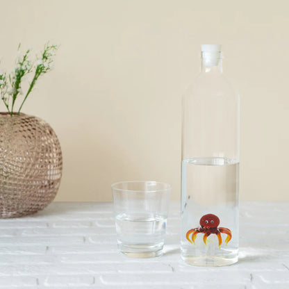 Atlantis Octopus bottle beside a glass full of water and a rattan vase