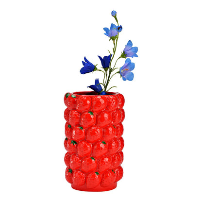 Strawberries vase in red with a stem of blue flowers placed inside.