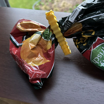Fries food clips a single yellow clip sealing an open bag of crisps on a wooden table.