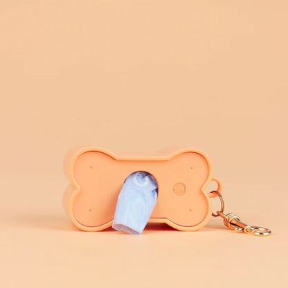 Biscuit dog waste bag holder in peach with a light-blue bag coming out of the opening
