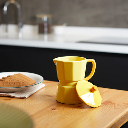 Yellow Moka mug on a wooden table with biscuits, lid resting beside it