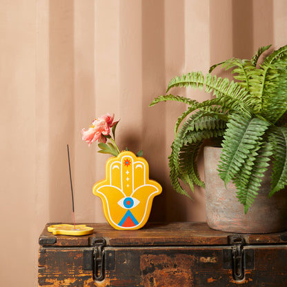 Yellow Lucky Hand vase with a pink flower on a wooden trunk
