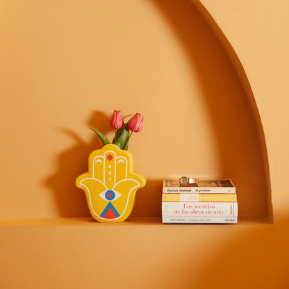 Yellow Lucky Hand vase with pink tulips on a shelf next to some books