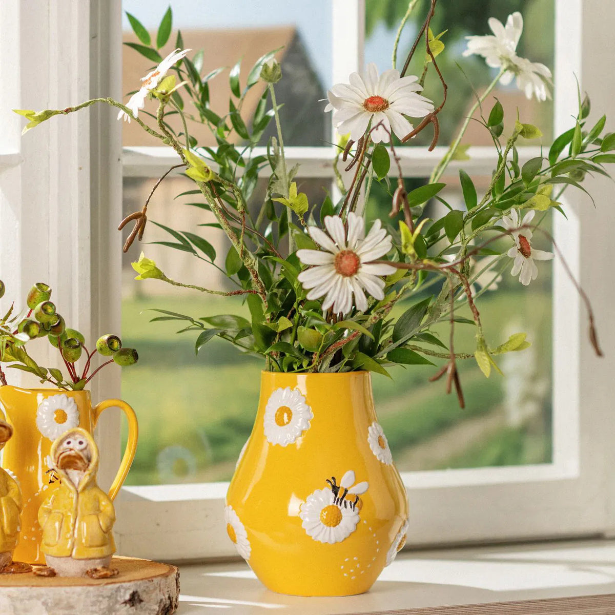Bee Happy vase shaped like a yellow jug with painted bees and daisies, filled with white flowers.