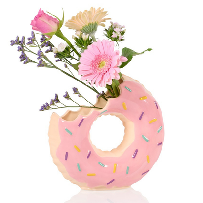 Doughnut vase in pink with a bunch of colourful flowers arranged in the bite opening.