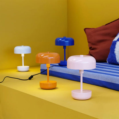 Four Haipot rechargeable lamps in different colours, lit on a yellow set next to a sofa.