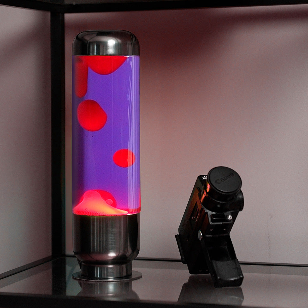 Lampada da Tavolo Lava Capsule: la lampada accesa su una mensola accanto a una fotocamera.