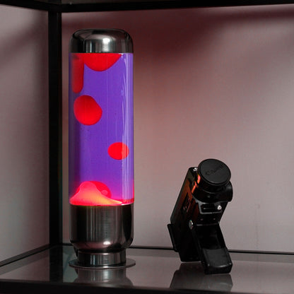 Lampada da Tavolo Lava Capsule: la lampada accesa su una mensola accanto a una fotocamera.