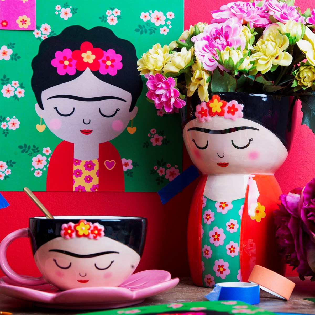 Vaso Frida accanto a una tazza coordinata e a un poster con quel volto, tra fiori colorati.
