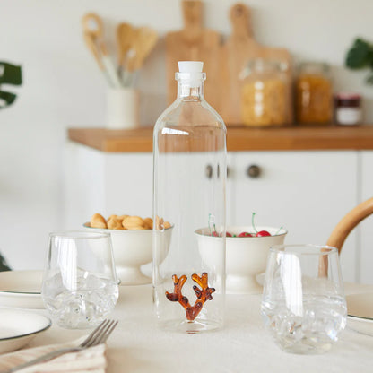 Atlantis Corallo bottle on a set table with glasses and bowls, kitchen in the background