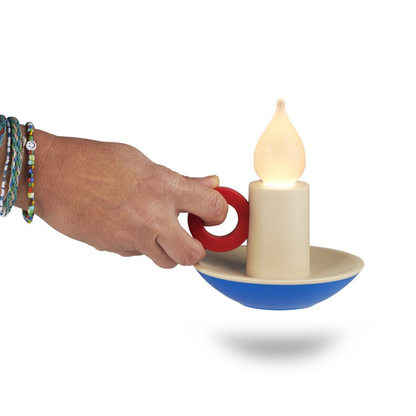 Candle Memphis lamp lit, held by hand using its red ring handle.