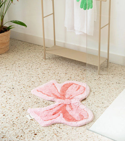 Soft bow rug in pink on the floor near a towel rack and a green plant
