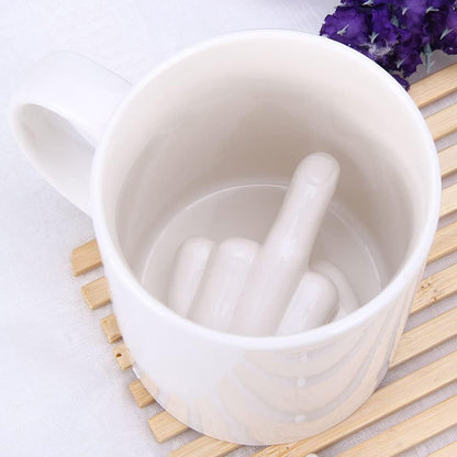 The middle-finger mug seen from above on a wooden trivet, among purple flowers
