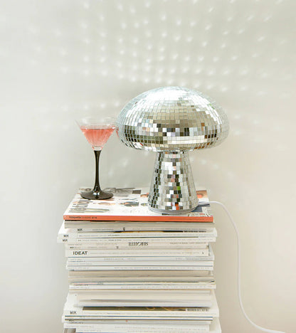 The mirrored mushroom lamp on a stack of magazines, next to a pink cocktail