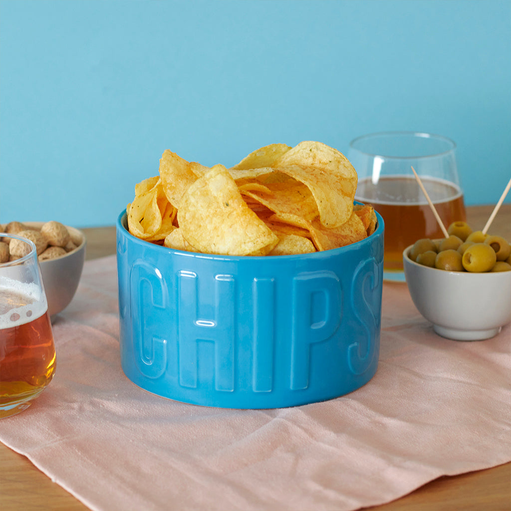 Ciotola Snack Chips azzurra piena di patatine, tra un bicchiere di birra e una ciotola di olive
