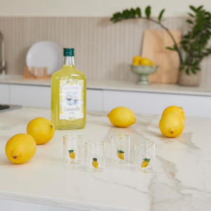 Lemon Shot Glass Set: the glasses on the marble counter with lemons and the bottle behind.