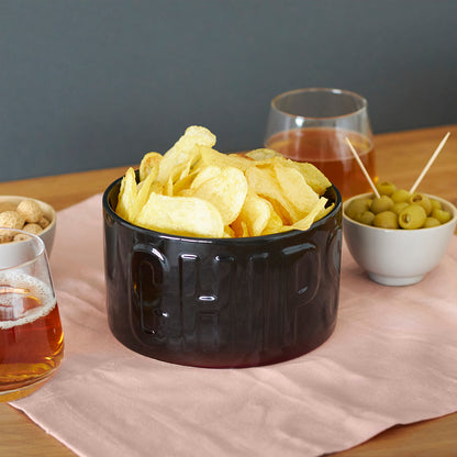 Ciotola Snack Chips nera piena di patatine, tra un bicchiere di birra e una ciotola di olive