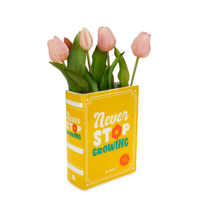 Yellow book-shaped vase reading Never Stop Growing, holding pink tulips