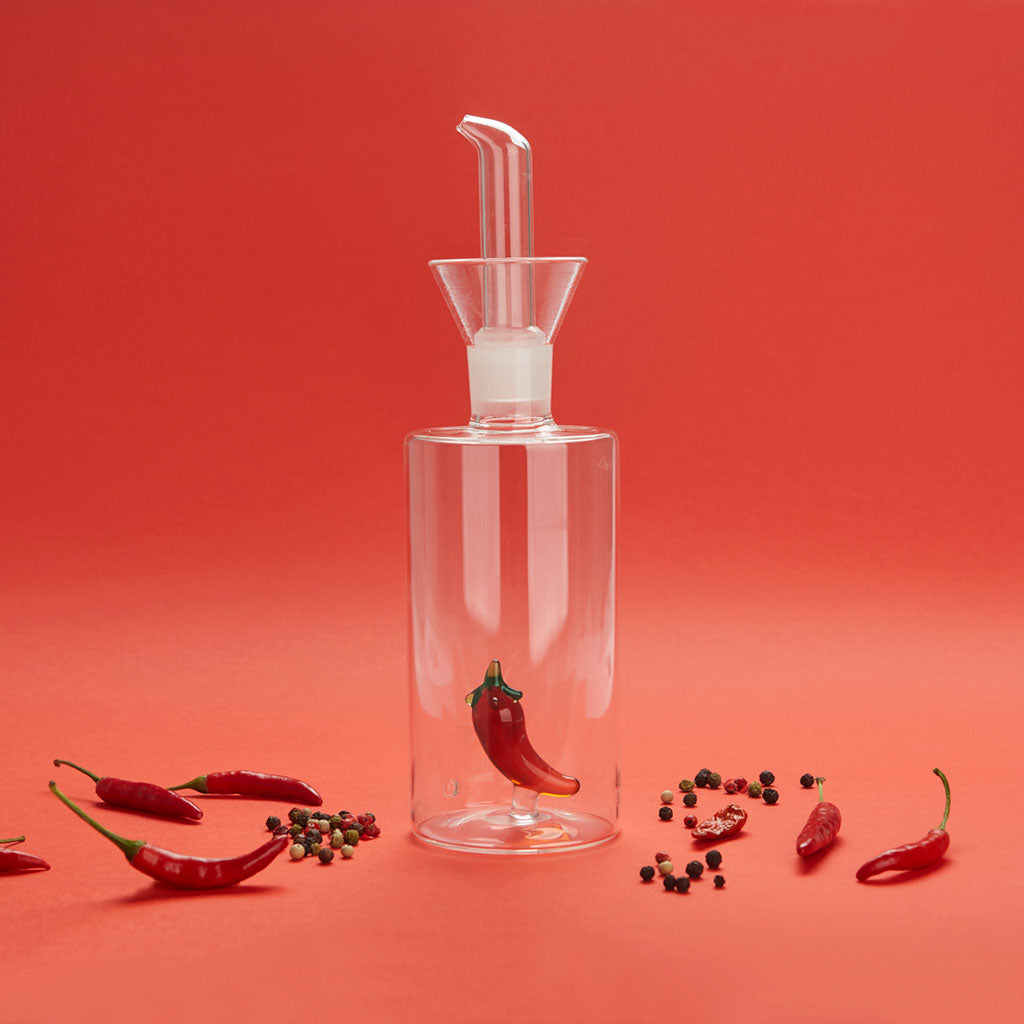 Oliera Chilli su sfondo rosso, circondata da peperoncini e grani di pepe
