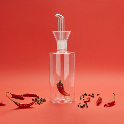 Oliera Chilli su sfondo rosso, circondata da peperoncini e grani di pepe
