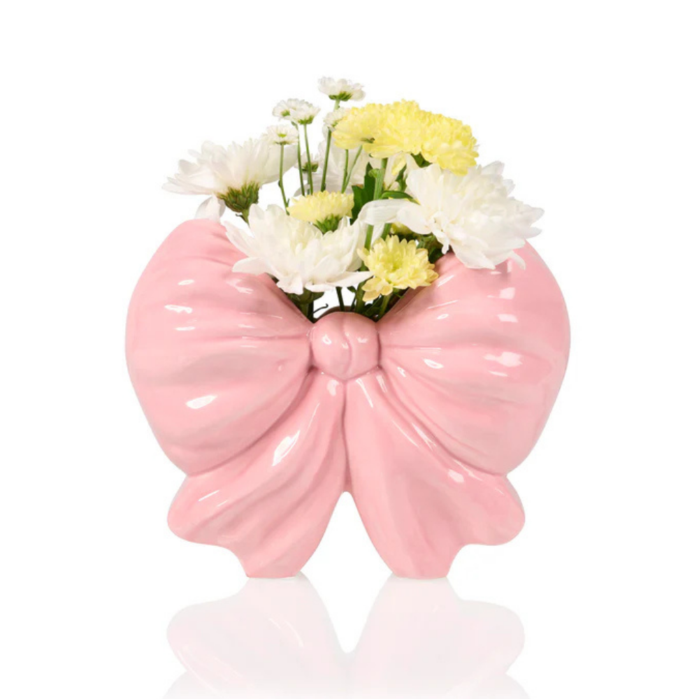 Vaso Fiocco: a glossy pink ceramic bow-shaped vase, holding white and yellow daisies.