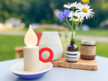 Candle Memphis lamp lit on an outdoor table, with daisies in a small jar nearby.