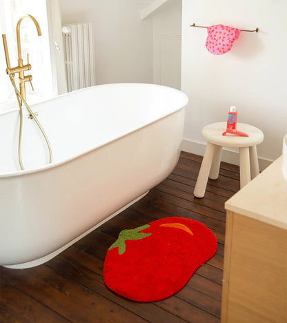 Tomato rug in red draped over the tub's edge, a stool with a pink bottle in the background