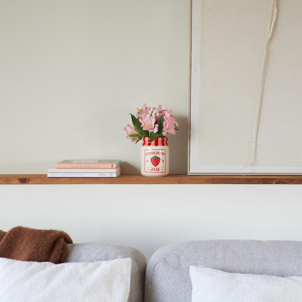 Jam vase, strawberry version on a wooden shelf, under a painting and above a grey sofa