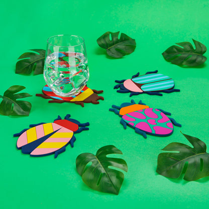 Beetle coasters placed under a wine glass, among leaves on a green background.