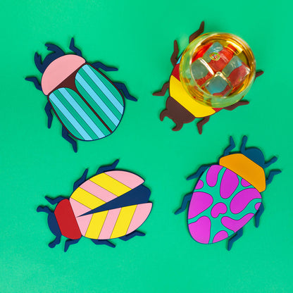 Beetle coasters placed under a glass of orange drink, among green leaves.
