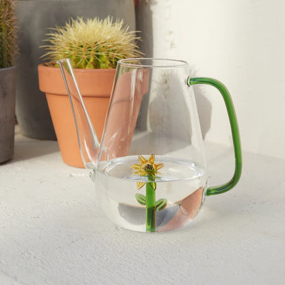 Botanical Sunflower watering can with the painted sunflower, filled with water next to a plant pot.