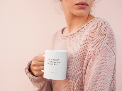Be Yourself mug in white, held by a person wearing a pink jumper.