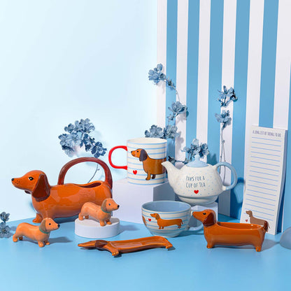 Dachshund catch-all vase styled with other dachshund pieces: a mug, teapot and figures, on stripes.