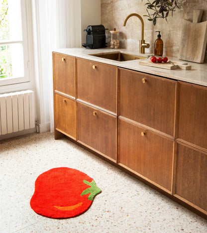 The red tomato rug placed in front of wooden kitchen cabinets
