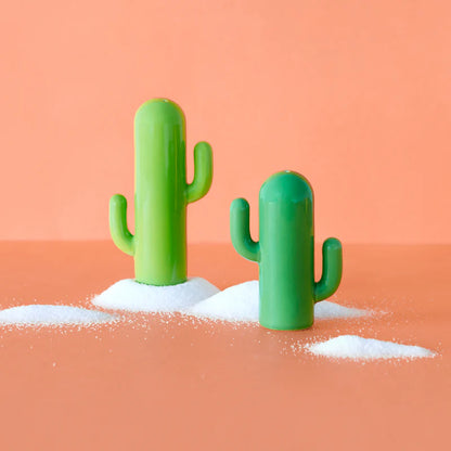 Cactus salt and pepper shakers resting on two small mounds of salt, on an orange background.