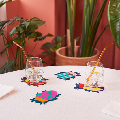 Beetle coasters placed under two glasses with straws, on a pink tablecloth.