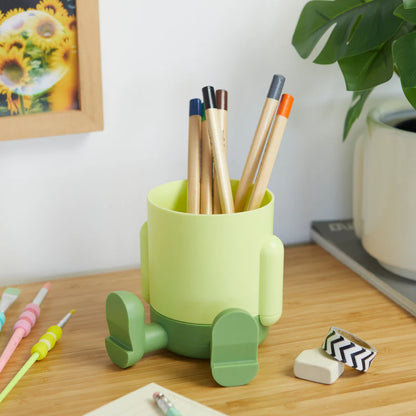 Mr.Sitty pen holder green pot on a wooden desk, with pencils, an eraser and a plant nearby.