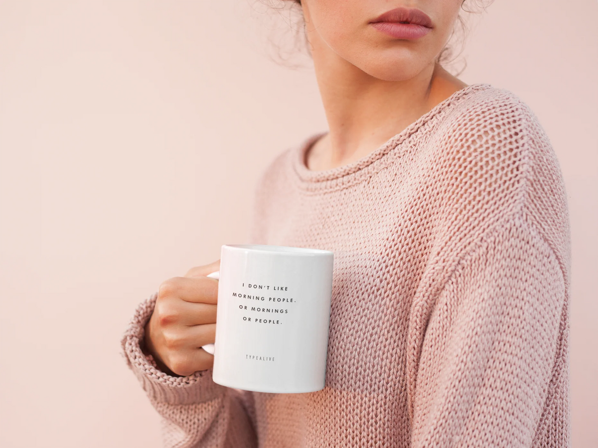 Morning People mug in white, held by a person wearing a pink jumper.