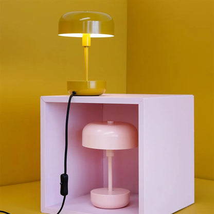 Haipot lamp in yellow, lit on a pink cube, with a second pink lamp below.