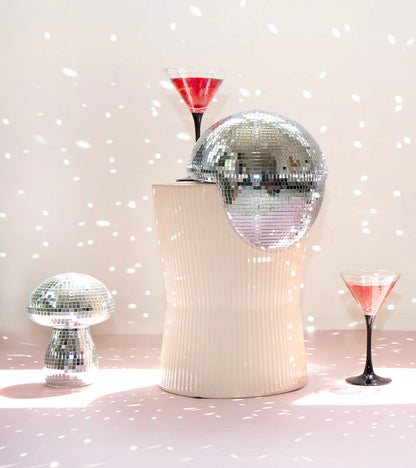Mini disco mushroom lamp on a white pedestal between two cocktail glasses