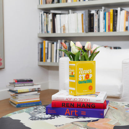 Yellow Book vase with pink tulips, on a stack of books in a living room with a bookcase