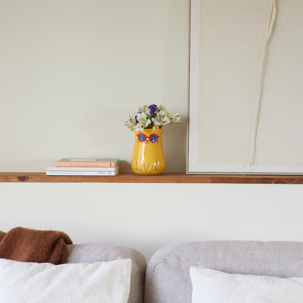 Cool Cat Vase: the yellow vase with flowers standing on a shelf in the living room.